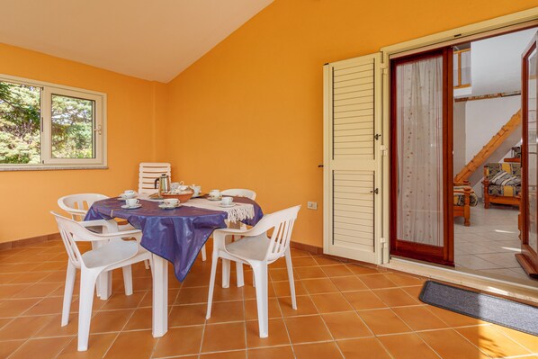 Un coin repas avec une table dressée pour quatre personnes, des chaises blanches et une fenêtre donnant sur les arbres.