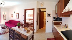 Un espacio habitable compacto con comedor, un sofá rojo, una cocina con cafetera y una cama al fondo.