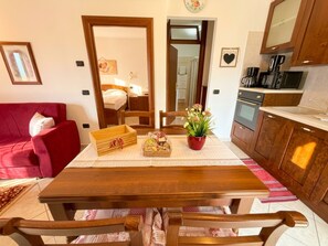 A compact living space with a dining table, chairs, a red sofa, a kitchen area, and a visible bedroom.