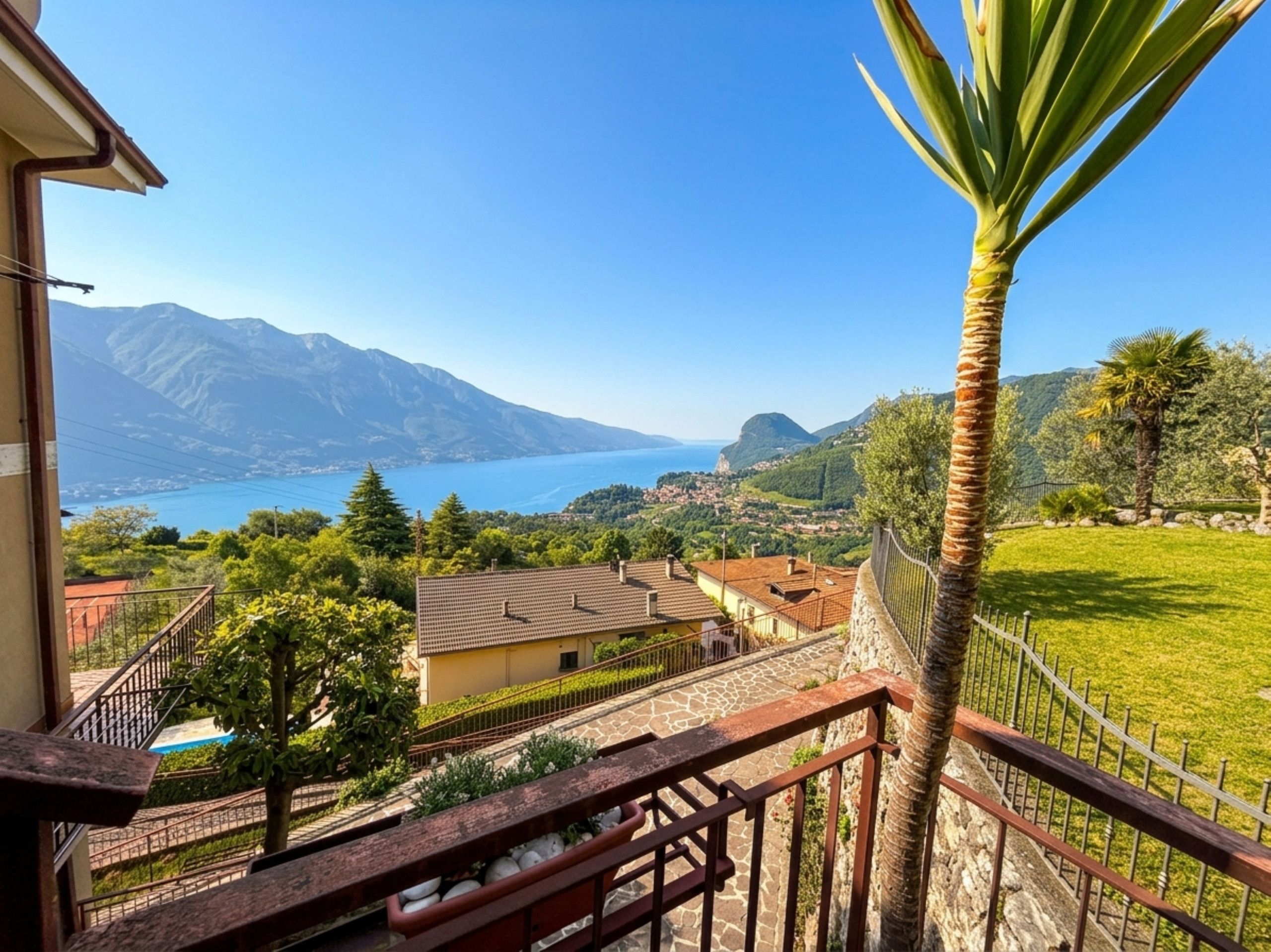 A balcony with a view of a lake, mountains, and a palm tree.
