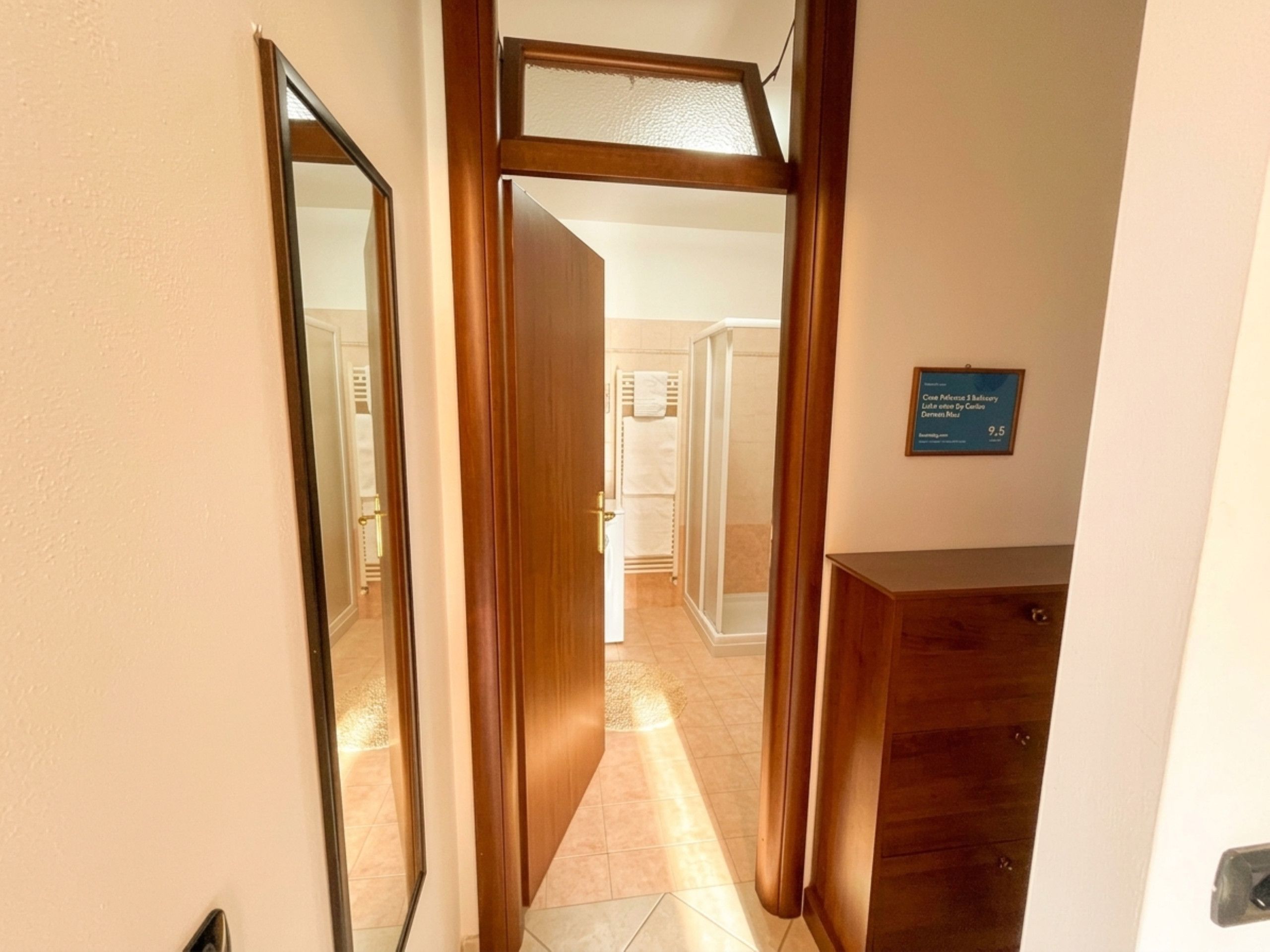 A hallway with a wooden door leading to a bathroom with a shower and a towel rack.