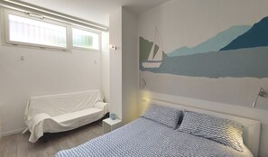 Quarto com cama, sofá branco, luminária na parede e janela com persianas.