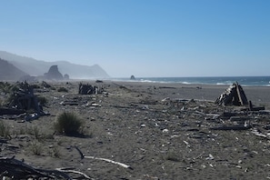 A beach with scattered debris and a clear view of the ocean and distant mountains. - Friends & Family Seaside Retreat, Walk to Beach! (Gold Beach)