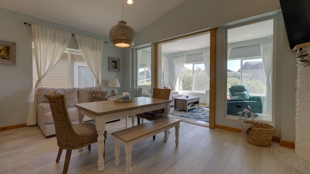 Un salon spacieux avec une table à manger en bois, des chaises en osier et un banc. Une grande fenêtre offre une vue sur l’extérieur.