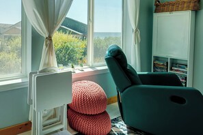 A room with a window, a white radiator, a teal chair, a red knitted pouf, and a bookshelf with books. - Friends & Family Seaside Retreat, Walk to Beach! (Gold Beach)
