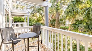 A covered outdoor seating area with a table and chairs, surrounded by a white railing and lush greenery. - Lagoon Villa 43 - Walk to Ocean! Prime Location! (Isle of Palms)
