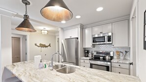 A modern kitchen with a marble countertop, stainless steel appliances, and pendant lighting. - Lagoon Villa 43 - Walk to Ocean! Prime Location! (Isle of Palms)