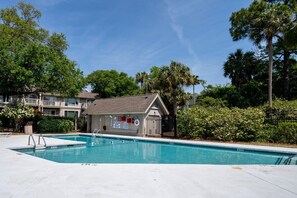 A swimming pool with a lifeguard station, surrounded by lush greenery and a two-story building with balconies.