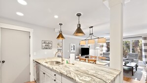 A modern kitchen with a marble countertop, pendant lighting, and a dining area with a TV and seating. - Lagoon Villa 43 - Walk to Ocean! Prime Location! (Isle of Palms)
