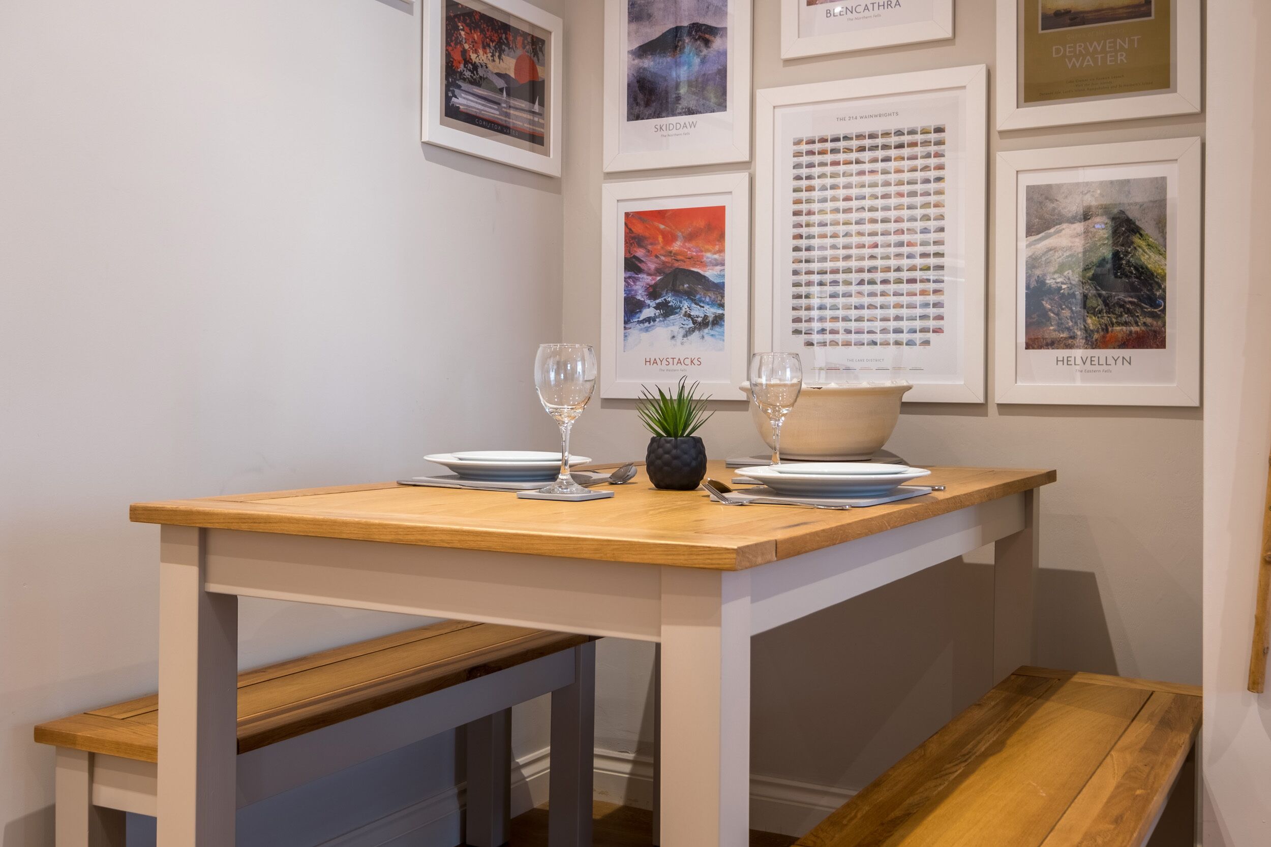A dining area with a wooden table set for two, accompanied by a small potted plant and two wine glasses.