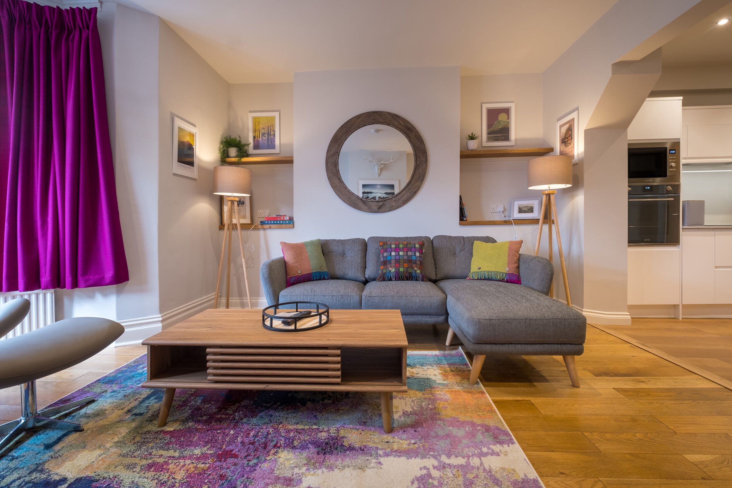 A modern living room with a grey sectional sofa, a wooden coffee table, and a colorful rug.