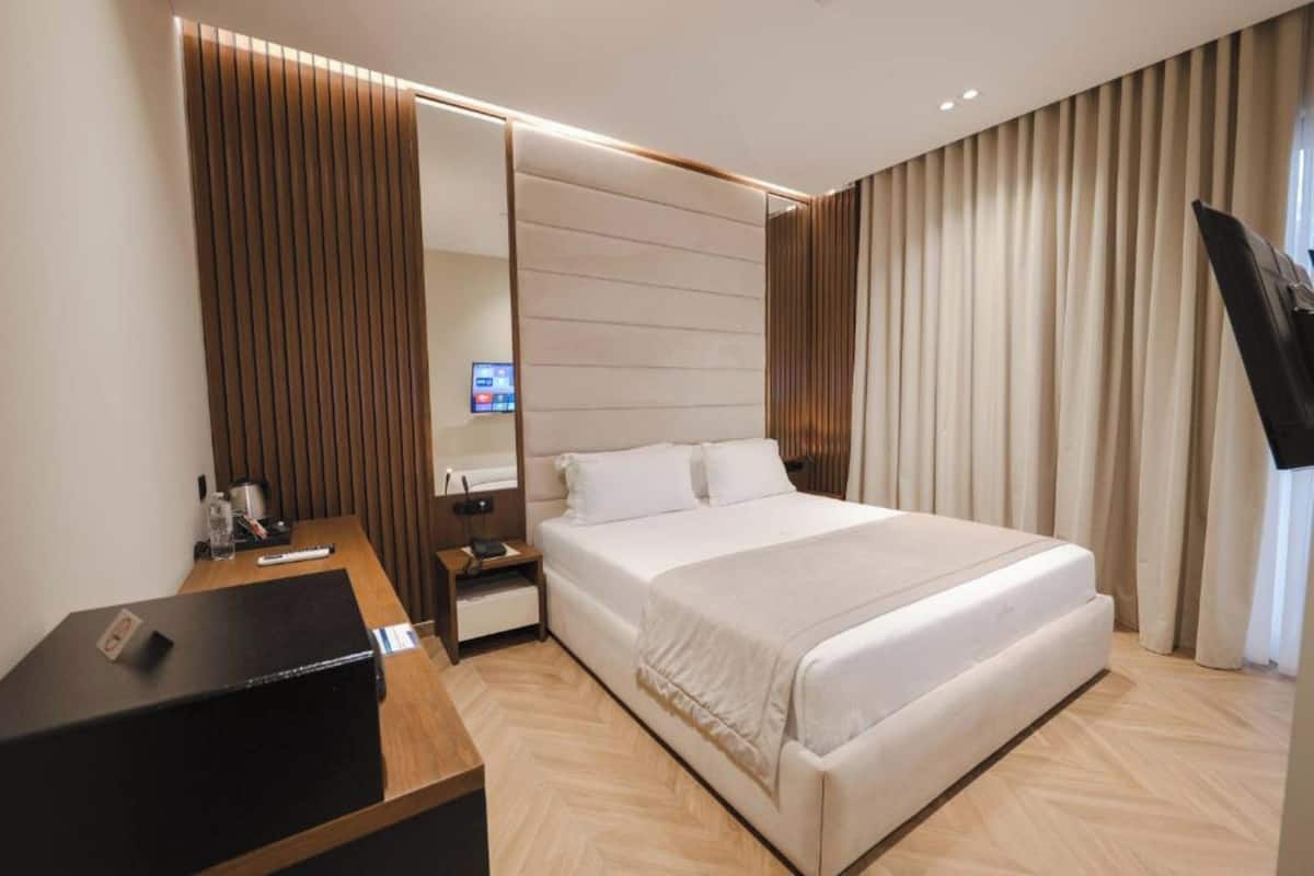 A modern hotel room with a large bed, a desk with a computer, a TV, and a mirror.