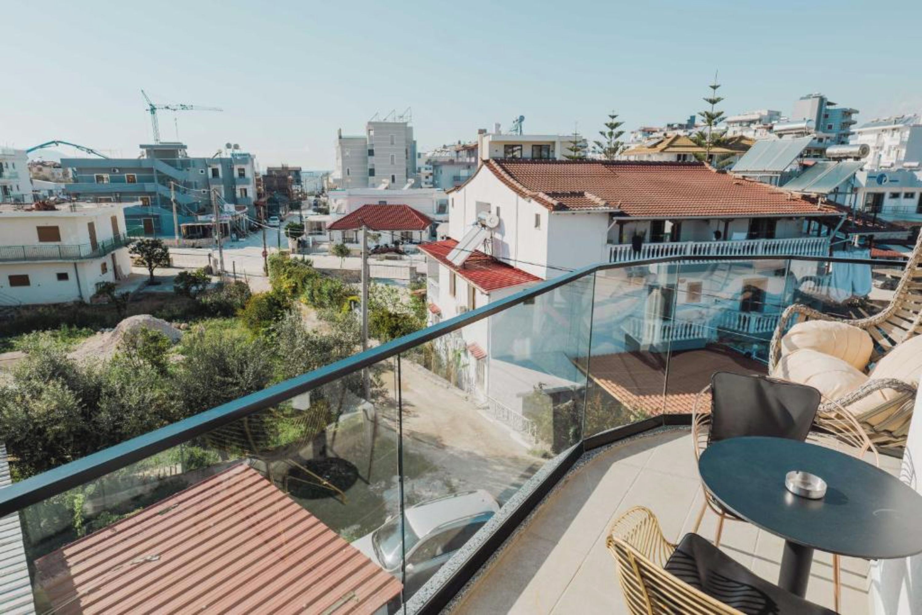 A balcony with a glass railing overlooking a residential area with houses and construction cranes.