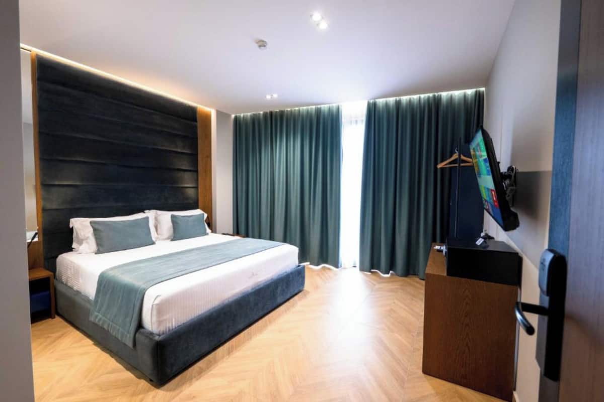A modern hotel room with a large bed, a wooden headboard, a flat-screen TV, and a wooden desk.