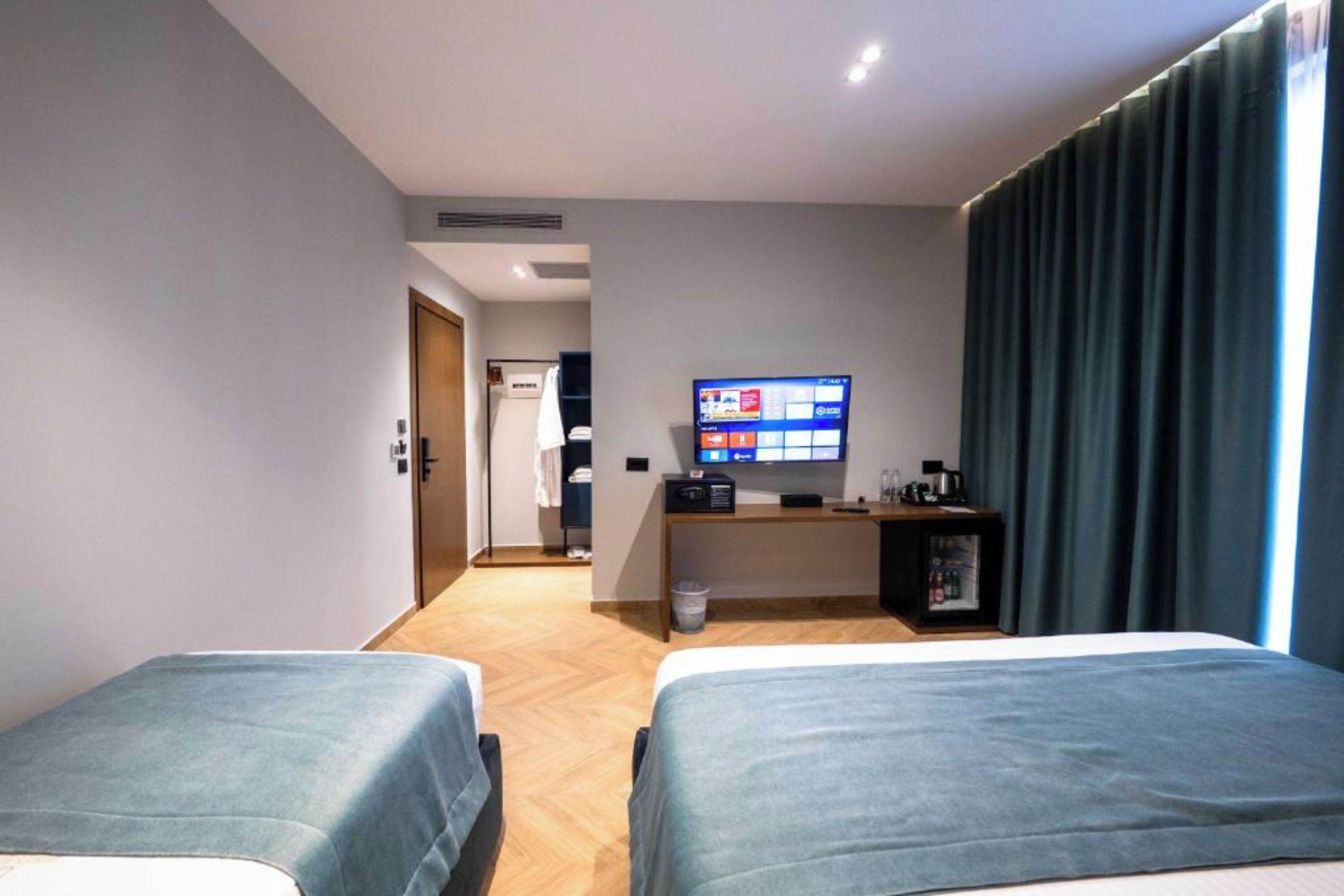 A hotel room with two beds, a TV, a desk with a computer, and a view of the hallway.