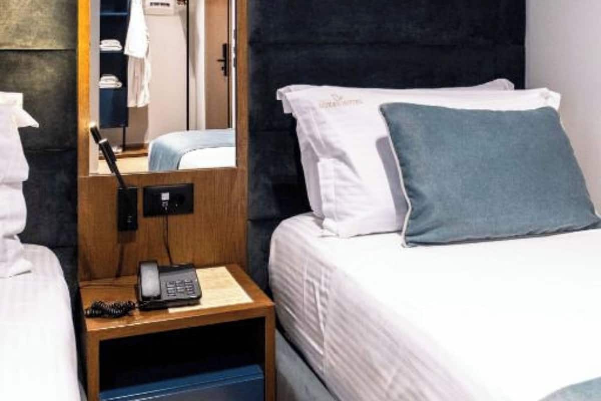 A hotel room with a bed, a bedside table with a phone, a mirror, and a wardrobe.