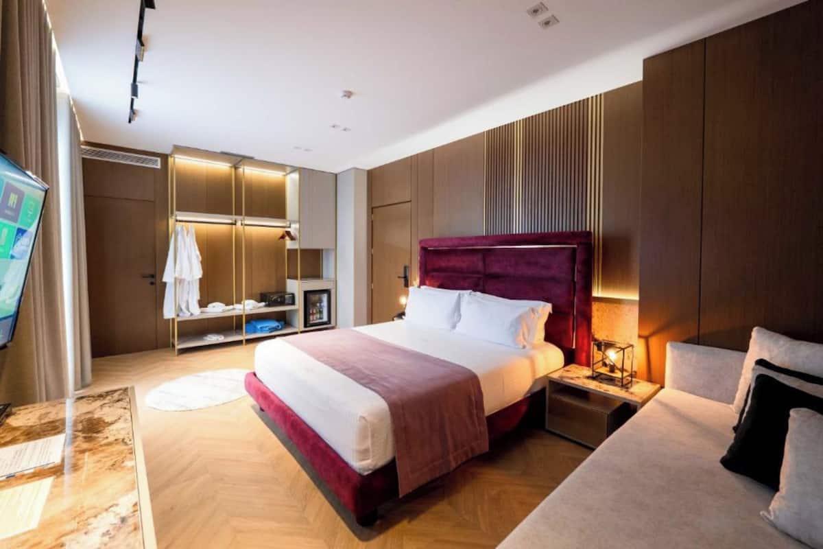 A modern hotel room with a large bed, a bedside table with a lamp, a wardrobe, and a television.