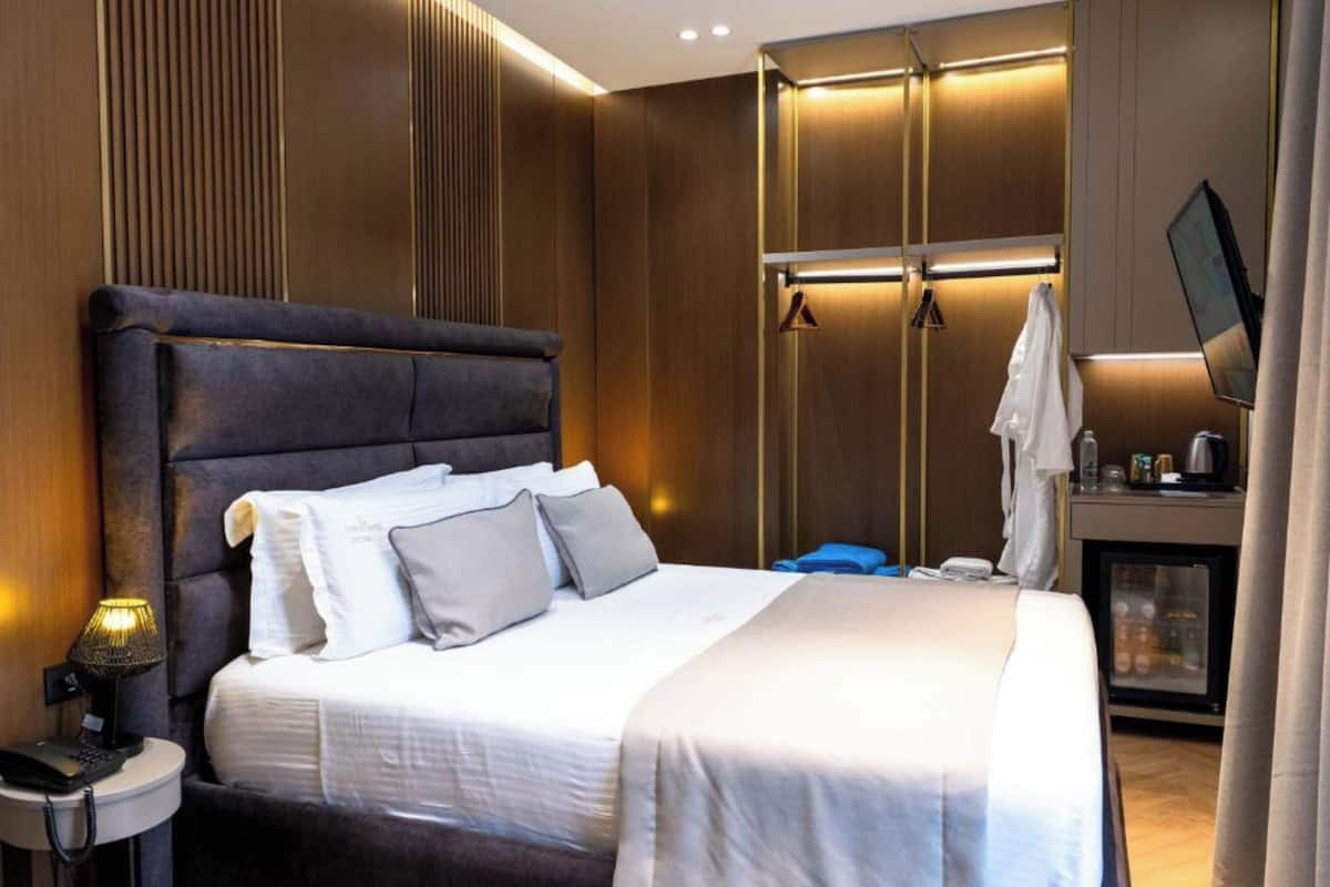 A modern hotel room with a large bed, bedside table, lamp, and a TV.