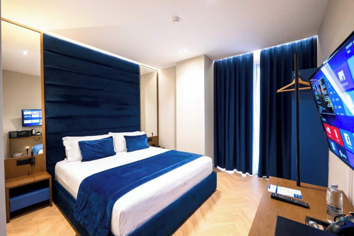 A hotel room with a large bed, a TV, a desk with a computer, and a wardrobe.
