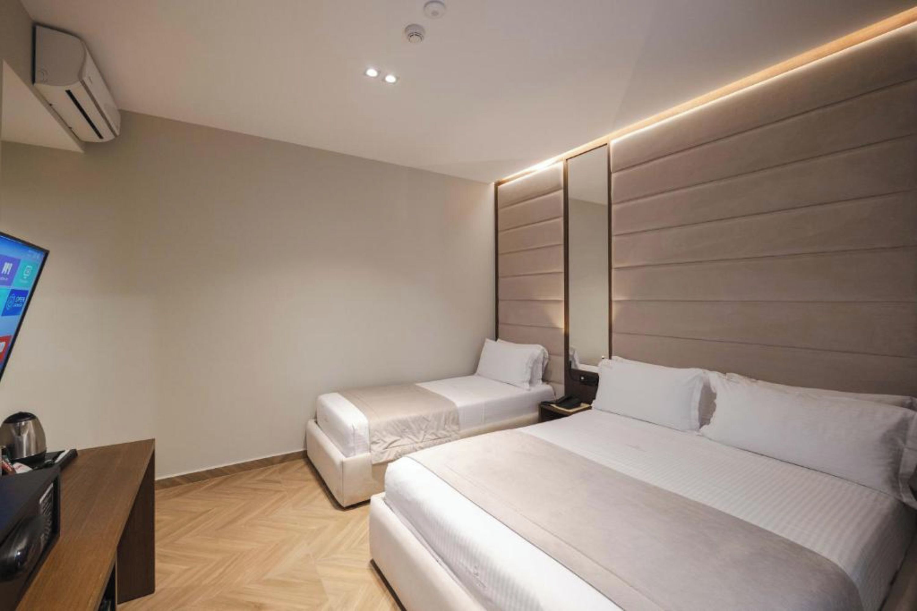 Quarto de hotel com duas camas, uma escrivaninha com computador e um espelho grande na parede.