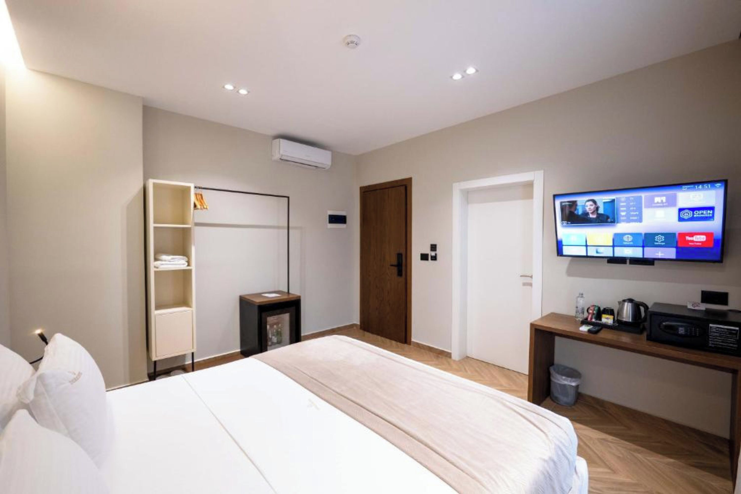 A hotel room with a bed, a TV, a desk with a coffee maker, a wardrobe, and a door.