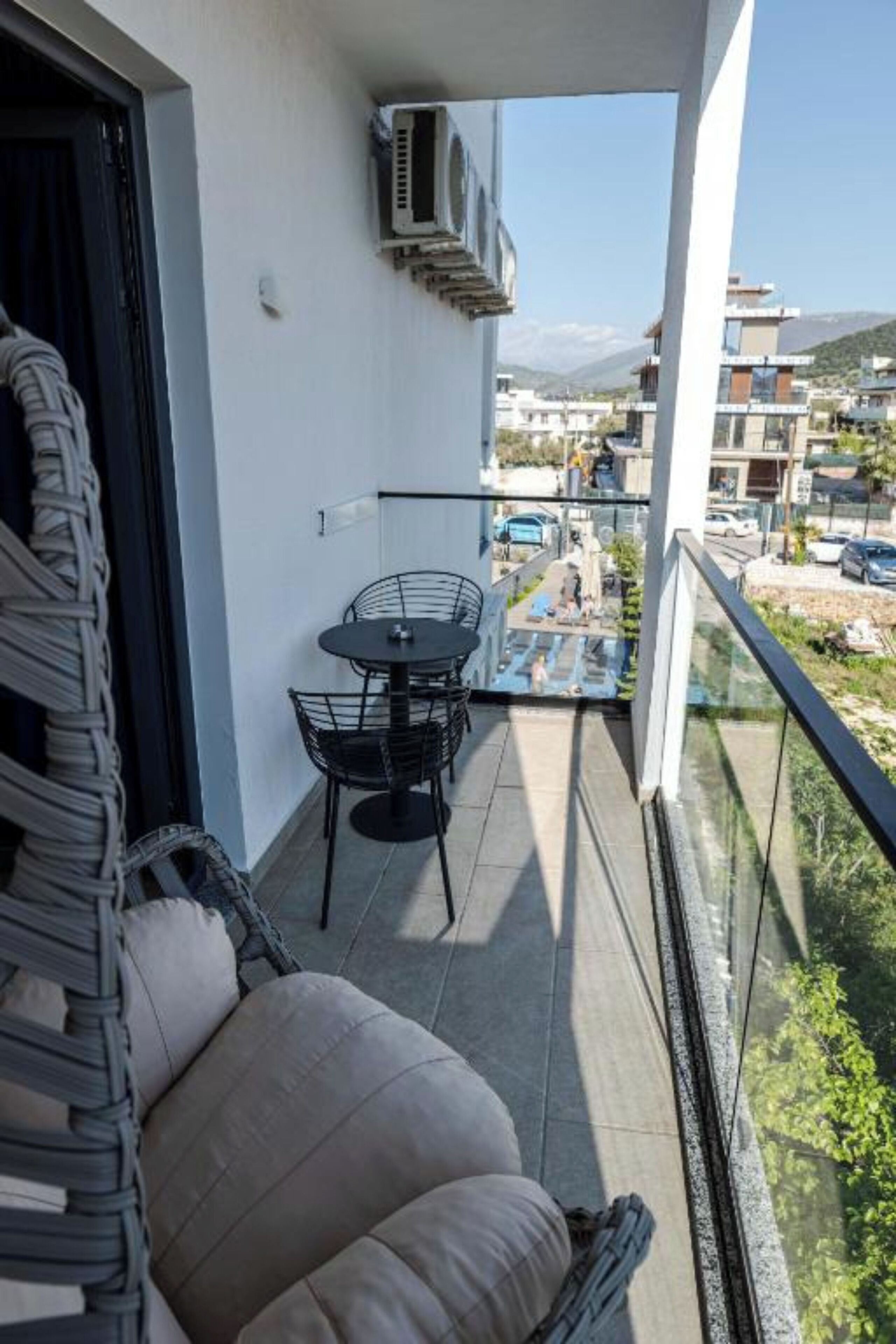 A balcony with a sofa, a table, and chairs, overlooking a residential area with buildings and a mountain in the distance.