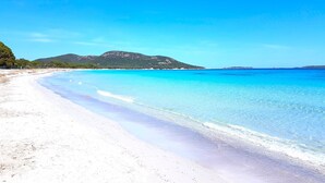 Ein Strand mit klarem türkisblauem Wasser, weißem Sand und einem Berg im Hintergrund.
