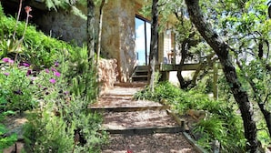 A stone staircase leading to a wooden deck surrounded by lush greenery and flowering plants. - Apartment for 2 to 4 people with 1 bedroom. (Porto-Vecchio)