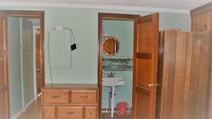 Une pièce comprenant une commode en bois, un miroir, un lavabo et une porte donnant sur une autre pièce.