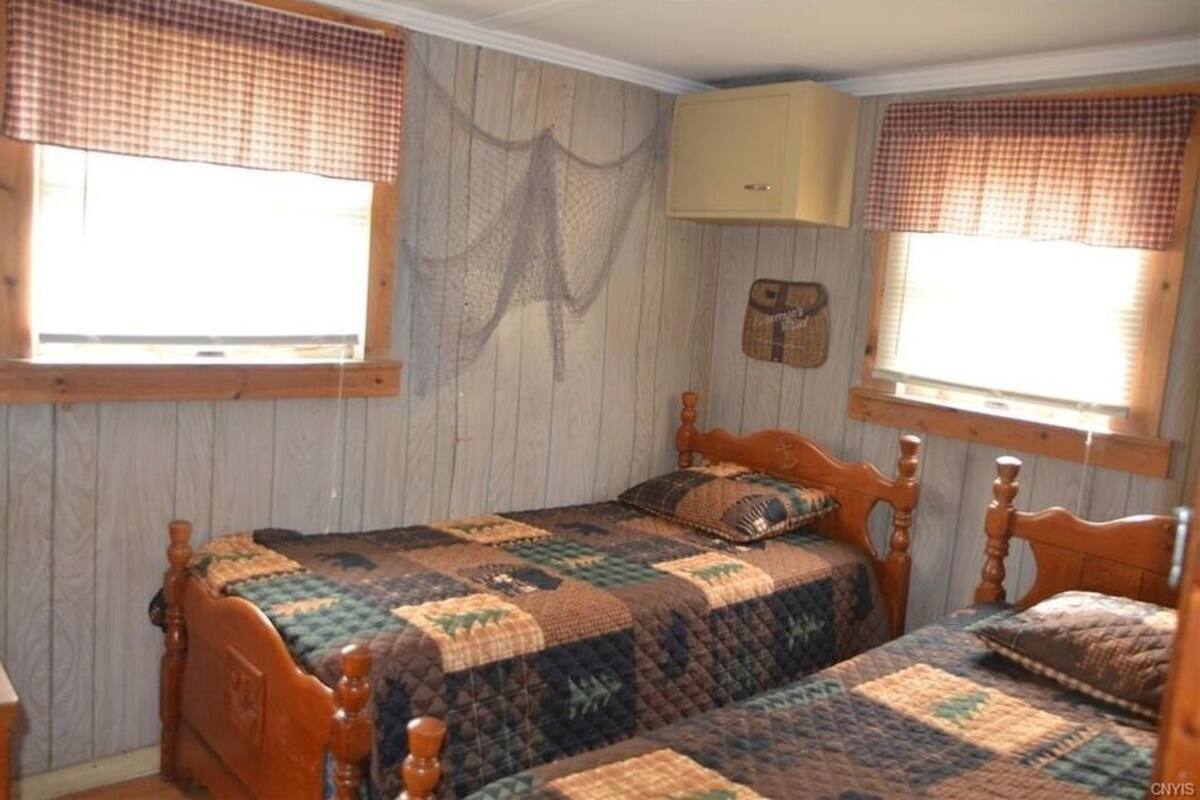 Ein Schlafzimmer mit zwei hölzernen Betten, einer gesteppten Tagesdecke, einem Holz-Kopfteil und einem Fenster mit karierter Vorhangbahn.