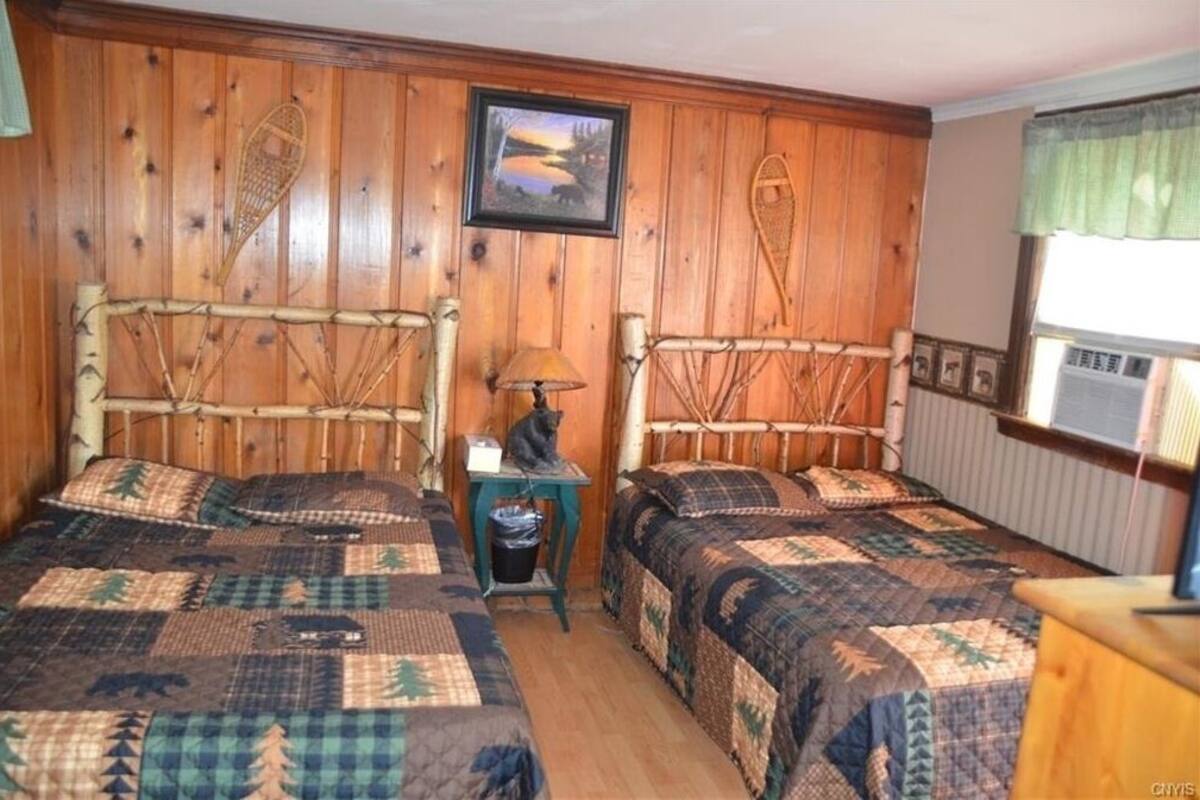 Ein Zimmer mit zwei Holzbetten, einem kleinen Tisch mit einer Lampe und einem Bild an der Wand.
