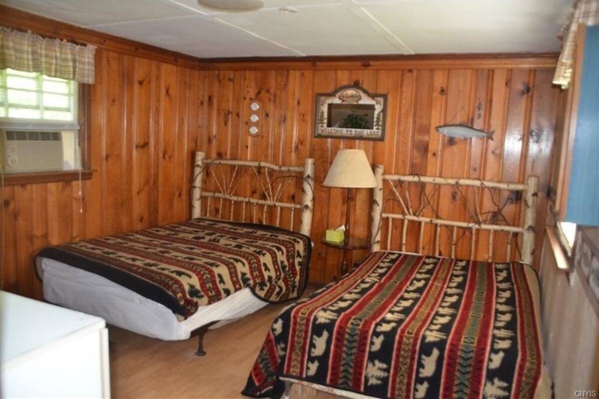 Eine Holzhütte mit zwei Betten, Holzwänden, einem aufgehängten Fisch und einem Willkommensschild.