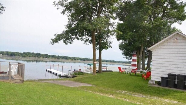Une propriété au bord du lac, dotée d’un quai, d’un petit abri et d’un bâtiment blanc surmonté d’un phare aux rayures rouges et blanches.