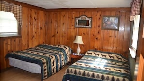 Une pièce aux murs lambrés, avec deux lits dotés de draps à motifs d’élan, une petite table avec une lampe, un panneau d’accueil encadré et un tableau accroché au mur.