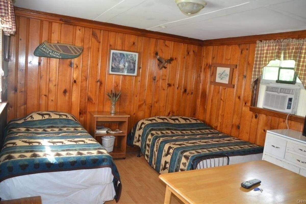 Eine Holzhütte mit zwei Betten, die mit Tierprint-Bettwäsche bezogen sind, einem kleinen Tisch und einem Vorhangfenster.