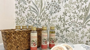 A set of hair care products including bottles and bars of soap, displayed on a table with a floral wallpaper background. - Juniper House via Mazzini (Torino)