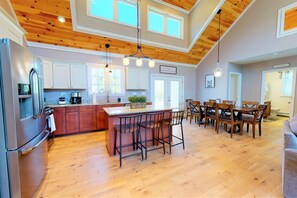 A spacious kitchen with wooden ceiling beams, a central island with bar stools, and a dining area with wooden chairs. - Gorgeous Conway Home A/C, Hot Tub & Full Game Room (Conway)