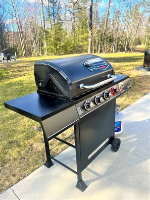 A portable gas grill with a side table, wheels, and a gas tank in the background. - Gorgeous Conway Home A/C, Hot Tub & Full Game Room (Conway)