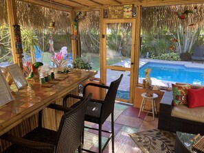 Relax in this tropical retreat with a dining table and wicker chairs, steps from a pool.