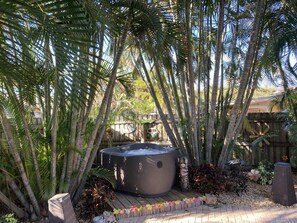 Relax in a serene garden oasis with a hot tub surrounded by lush tropical plants and a wooden deck.