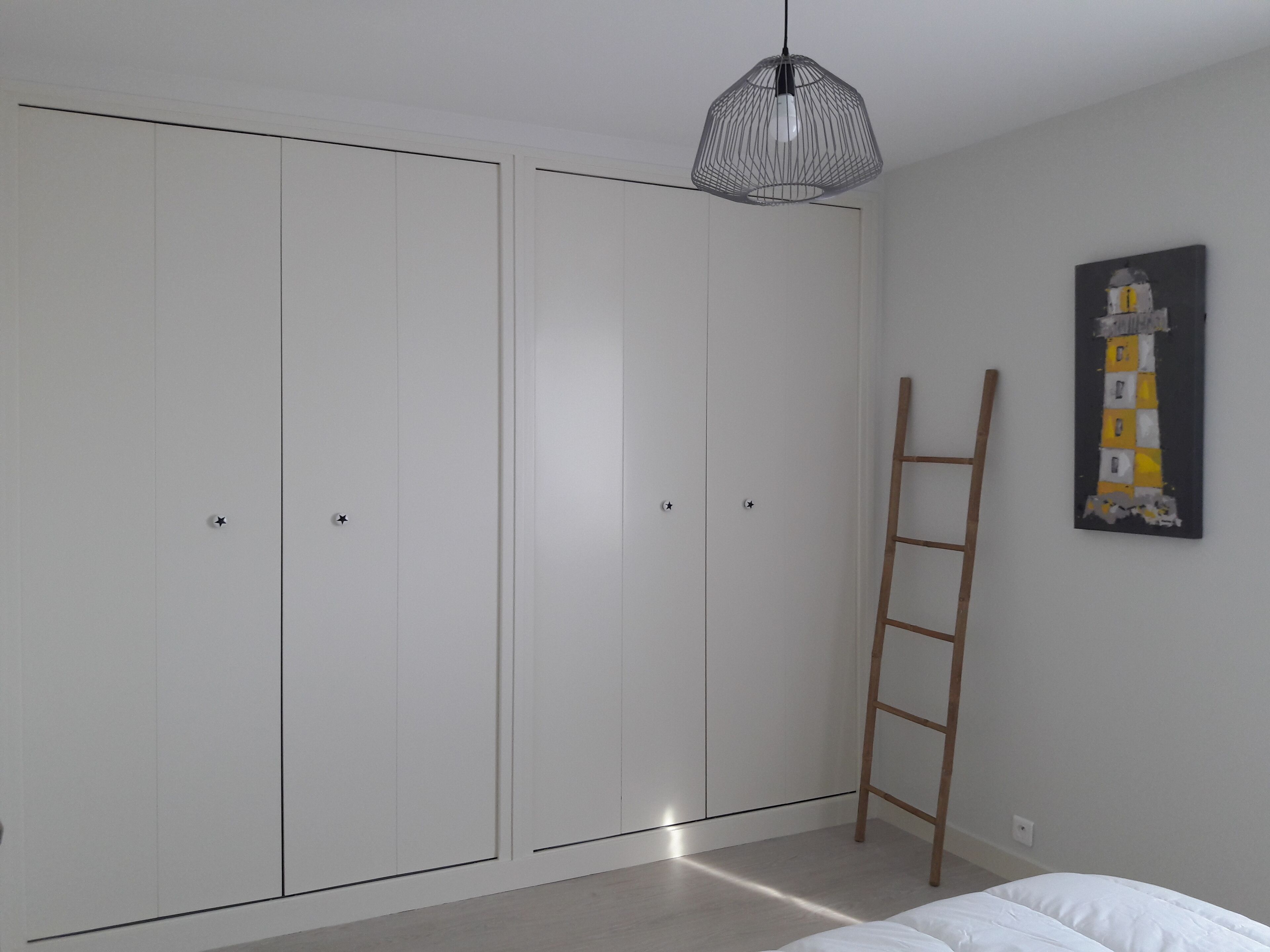 Une chambre avec une armoire blanche, une échelle en bois et un tableau accroché au mur.