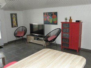 A room with a TV, two black wire chairs, a red cabinet, and a bed.