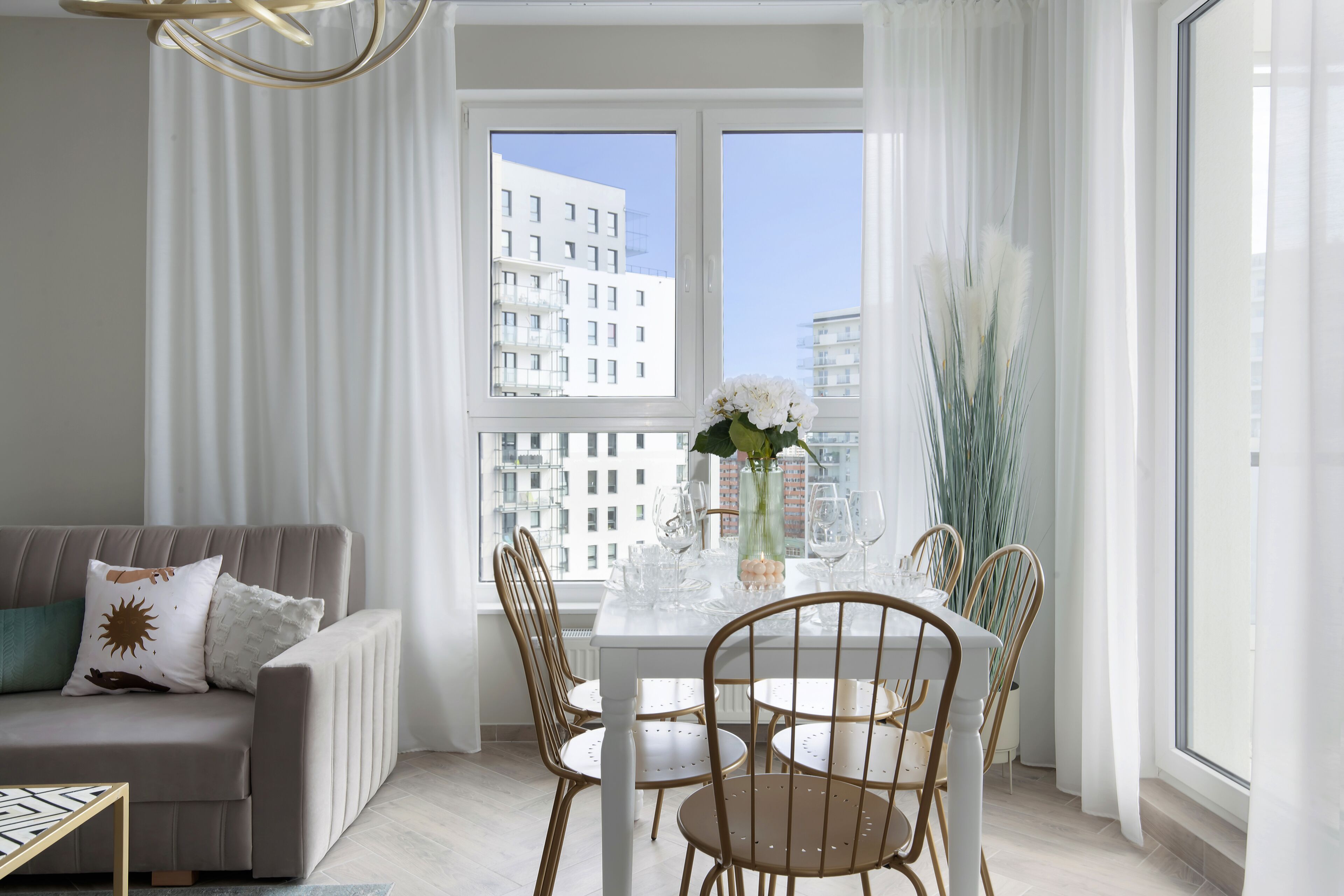Ein modernes Wohnzimmer mit einem weißen Sofa, einem Esstisch mit Stühlen und einem großen Fenster mit Blick auf die Stadt.