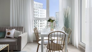 A modern living room with a white sofa, a dining table set with chairs, and a large window with a city view.