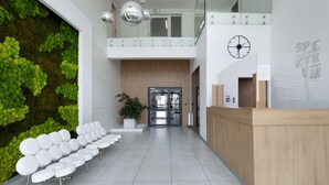 A modern reception area with a green wall, white chairs, a wooden reception desk, and a clock on the wall.