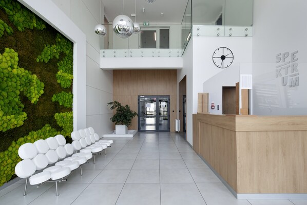 A modern reception area with a green wall, white chairs, a wooden reception desk, and a clock on the wall.
