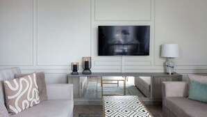 A modern living room with a flat-screen TV mounted on the wall, a console table with decorative items, and two sofas with patterned cushions.