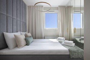A modern bedroom with a large bed, a view of the sky through a window, and a mirror reflecting the room.