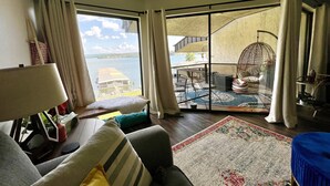 A living room with a large sliding glass door leading to a balcony with a view of a lake and a building across the water.