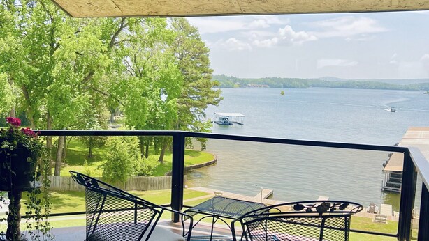 A balcony with two metal chairs and a table, overlooking a lake with a boat and dock.